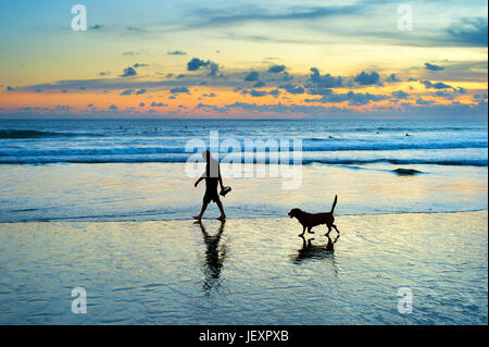 Silhouette of a man and dog walking on a beach at sunset. Bali island, Indonesia