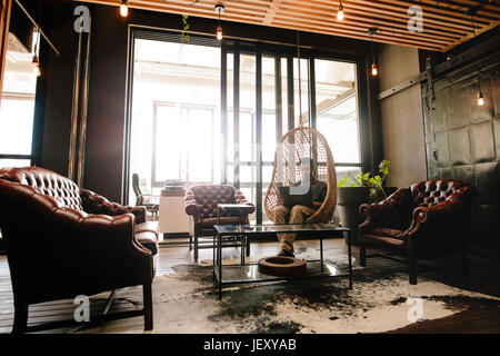 Young businessman sitting in a modern corporate environment. Man relaxing in office lounge and working on laptop computer. Stock Photo