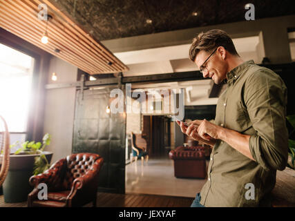 Side view of handsome young man reading text message on his mobile phone and smiling. Creative businessman using cell phone during break. Stock Photo