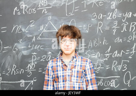 Teenager Boy in glasses, blackboard filled with math formulas background Stock Photo