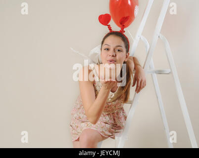 cute beautiful girl blowing you a kiss while sitting on the stairs, happy Valentine's day, holiday concept Stock Photo