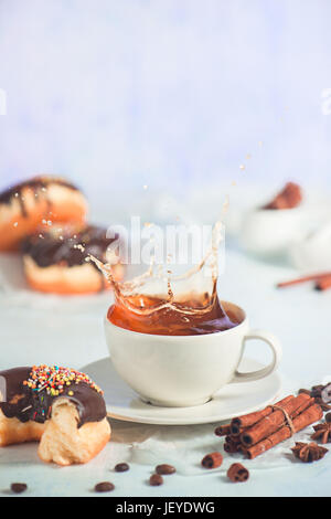 Coffee splash in a cup with chocolate glazed donuts on a white wooden background Stock Photo