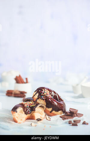 Chocolate glazed donuts with sprinkles and cinnamon on a white wooden background Stock Photo