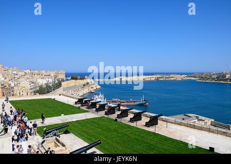 Soldiers preparing the cannons ready for the Noon Gun in Upper Barrakka Gardens with views across the Grand Harbour towards Fort Rikasoli and tourists Stock Photo