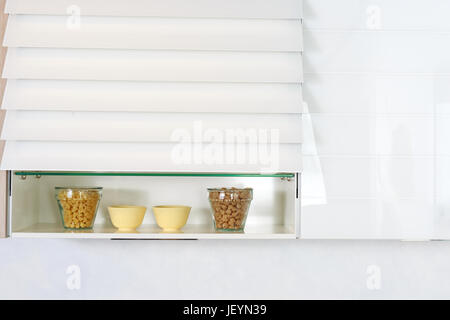 Food ingredients organized on a shelf on modern kitchen countertop. White simple kitchen. Stock Photo