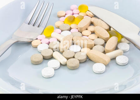 A mixture of pills on a light blue plate with a knife and fork. Stock Photo