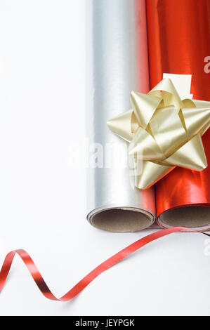 Overhead close up shot of two rolls of Christmas wrapping paper and a gold decorative rosette.  A swirl of shiny red ribbon is placed at the bottom of Stock Photo