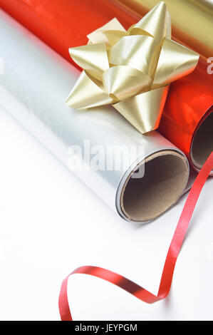 Close up, angled shot of gift wrapping paper rolls, rosette and ribbon on a white surface. Stock Photo