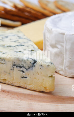 Close up of cheese selection on wooden board with crackers in soft focus background.  Focus is on French blue veined cheese. Stock Photo