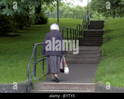 senior citizen  or old person seniors in Glasgow Scotland walking alone up stairs in park carrying shopping bags Stock Photo