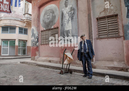 Havana, Cuba - December 12, 2016:  Street portrait of an old cuban man in downtown Havana, Cuba. In the background some beautiful paintings on the hou Stock Photo