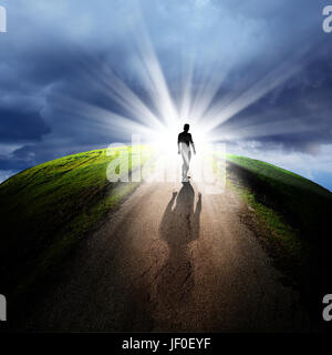 conceptual image of silhouetted man on empty road over cloudy sky with beam of light Stock Photo