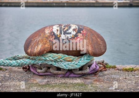 Rusty mooring post on the quay of Aarhus harbor in Denmark, with the number 12 painted on in a cirkel Stock Photo