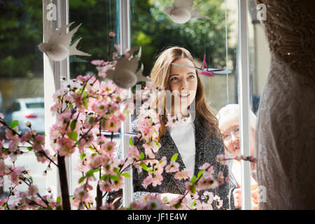Two women, a young woman and a mature woman looking through the window at a dress on display in a bridal boutique. Stock Photo