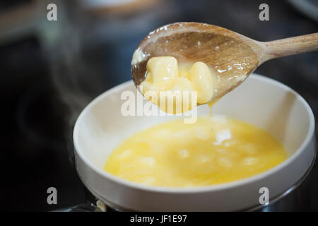 Close up of butter dripping from a wooden spoon into a bowl, steam. Stock Photo