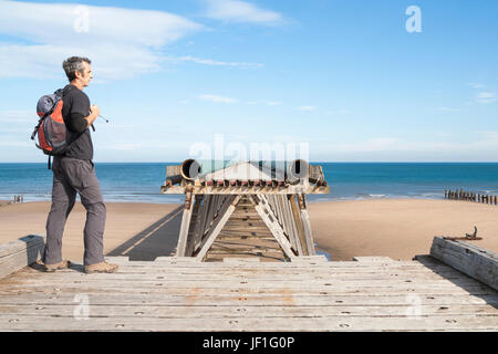 Hiker walking the England coast path standing on section of Steetley pier on North Sands beach at The Headland, Hartlepool, England. UK Stock Photo