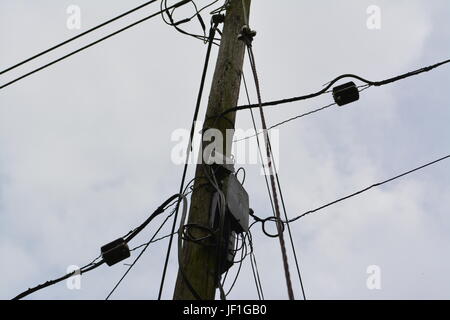 close up of electricity power and telephone cables wires on timber wooden pole with overcast grey cloudy sky in the background England UK Stock Photo