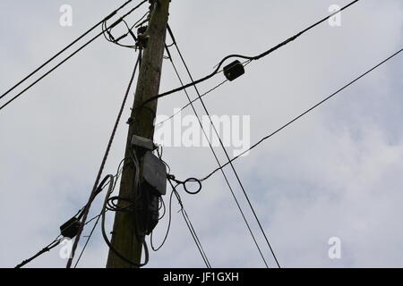close up of electricity power and telephone cables wires on timber wooden pole with overcast grey cloudy sky in the background England UK Stock Photo