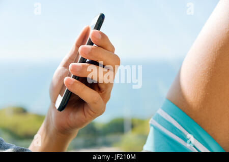 closeup of a young caucasian man in swimsuit using a smartphone outdoors, with the ocean in the background Stock Photo