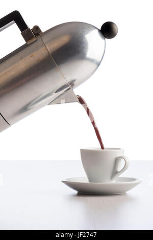 pouring coffee from coffeepot into white coffee cup, on white table. Stock Photo
