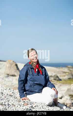 Smiling woman sitting on pebble beach Stock Photo