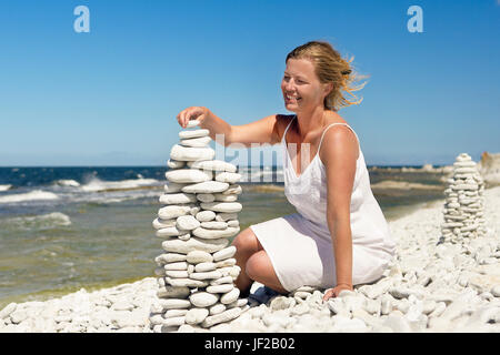 Woman on beach stacking stones Stock Photo