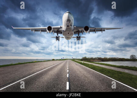 Airplane and road. Landscape with big white passenger airplane is flying in the cloudy sky over the asphalt road. Journey. Passenger airliner is landi Stock Photo
