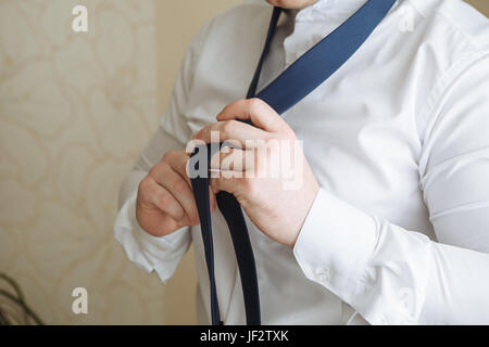 People, business, fashion and clothing concept - close up of man in shirt dressing up and adjusting tie on neck at home. Businessman putting on a tie. Stock Photo