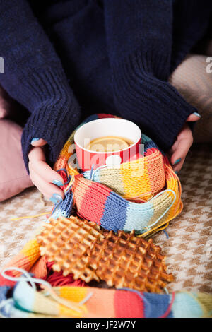 Cup of hot tea wrapped in knitted scarf holding by hands, top view diagonally winter cozy mood. Copyspace. Stock Photo