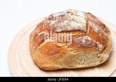 Elevated view of a fresh, uncut loaf of bread, resting on a light wood chopping board. Stock Photo