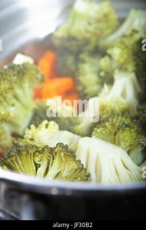 Broccoli florets and carrots cooking in a steamer, with steam visible.  Vertical (portrait) orientation. Stock Photo