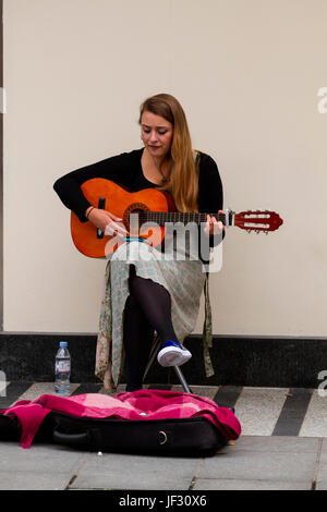 A female student busker sitting playing an acoustic guitar and singing outside the Marks & Spencer store along the Murraygate in Dundee, UK Stock Photo