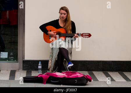 A female student busker sitting playing an acoustic guitar and singing outside the Marks & Spencer store along the Murraygate in Dundee, UK Stock Photo