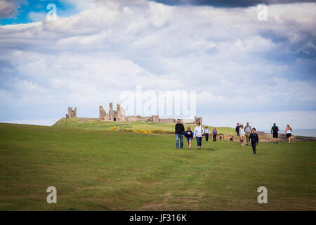 Tourists walking towards Dunstanburgh Castle from Craster, Northumberland, England. Stock Photo