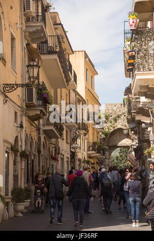People walking past shops and buildings near arch in busy pedestrianised shopping street Corso Umberto, Taormina, Province of Messina, Sicily, Italy. Stock Photo