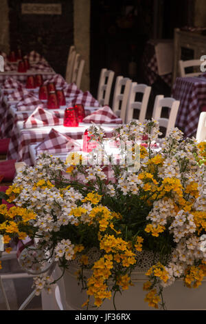 Flowers in front of Al fresco dining tables set with red checked cloths and chairs outside restaurant in Taormina, Province of Messina, Sicily, Italy
