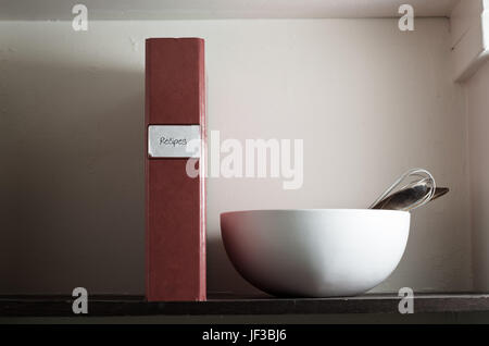 A slightly battered recipe file on an old larder shelf with mixing bowl and utensils.  Conceptual image for home cooking and family recipes.  Copy spa Stock Photo
