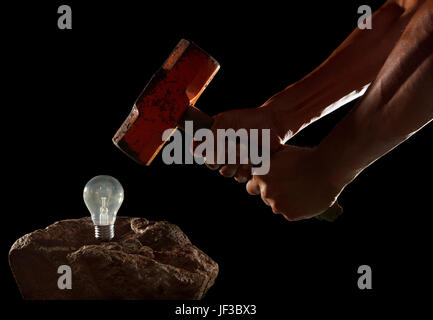 abstract of hand holding heavy hammer to breaking light bulb on the rock isolated on black Stock Photo