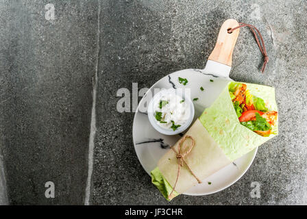 Mexican food. Healthy eating. Wrap sandwich: green lavash tortillas with spinach, fried chicken, fresh greens salad, tomatoes, yoghurt sauce. Dark sto Stock Photo
