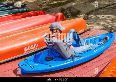 Teenager relaxing in the sun in a kayak (on dry land) at cabins in Jasper National Park, Alberta, Canada.