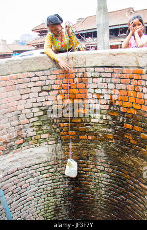 nepali woman drawing water from a well in the back streets of bhaktapur