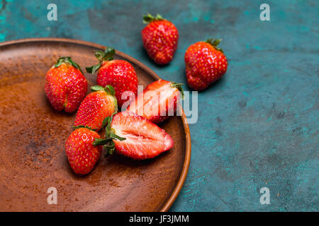 whole and sliced fresh red strawberries in ceramic plate on tabletop Stock Photo