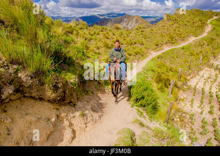 QUITO, ECUADOR - NOVEMBER, 25 2016: Unidentified young tourist riding a horse trought a sandy path near Quilotoa inactive volcano. Quilotoa is the wes Stock Photo