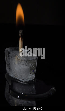 A lit match frozen inside an ice cube on a black acrylic surface. Stock Photo