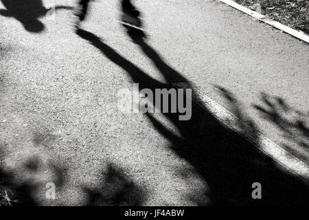 Abstract blurry shadows and silhouettes of two kids speeding on roller blades chasing one another and having fun in the park lane on summer vacation Stock Photo