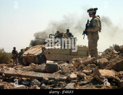 050326-N-6501M-022  U.S. Army soldiers and a Bradley Fighting Vehicle with the 2nd Battalion, 11th Armored Cavalry Regiment cautiously advance into a bunker area as they conduct a raid on the Hateen Weapons Complex in Babil, Iraq, on March 26, 2005.   The 11th Armored Cavalry is attached to the 155 Brigade Combat Team headquartered in Tupelo, Miss.  DoD photo by Chief Petty Officer Edward Martens, U.S. Navy.  (Released) Stock Photo