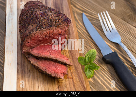 A large piece of grilled top sirloin sits on cutting board sliced and peppered Stock Photo