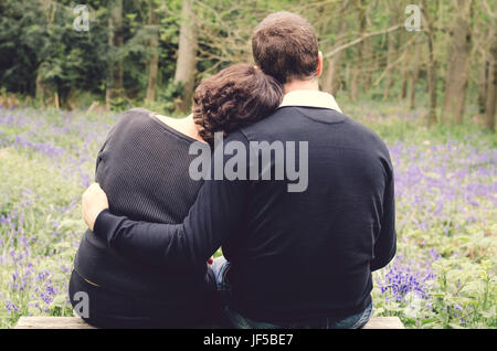 Loving couple sitting on the park bench surrounded by bluebell flowers. Stock Photo