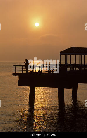 Dramatic sunset in fog over Puget Sound with waterfront fishing pier and silhouetted fisherman with fishing pole Seattle, Washington State USA Stock Photo