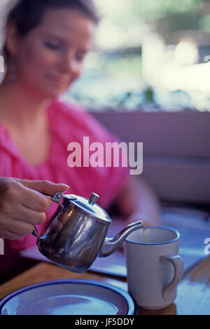 Woman sitting in cafe pouring  a cup of tea and smiling along the "Ave" University District Seattle Washington State USA Stock Photo